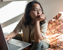 A woman rests her chin on her hand and stares away from her laptop.