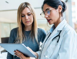 A woman and her doctor look at a tablet.