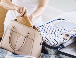 A woman packing a handbag and carry-on.