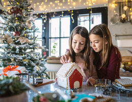 Two girls decorate a gingerbread house.