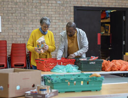 A man and woman fill a basket at a food pantry.