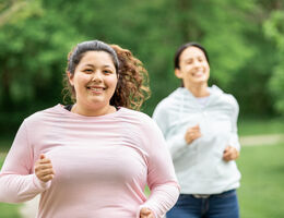 A woman jogs with another jogger in the background.
