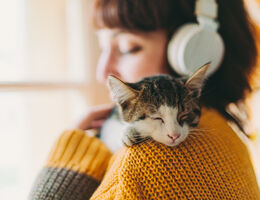 A woman with headphones on cuddles a kitten.