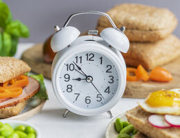 Alarm clock surrounded by plates of food and a cutting board.